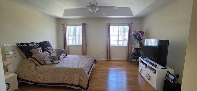 bedroom featuring ceiling fan, baseboards, a tray ceiling, and wood finished floors