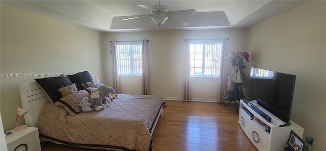 bedroom with ceiling fan, a tray ceiling, and hardwood / wood-style floors