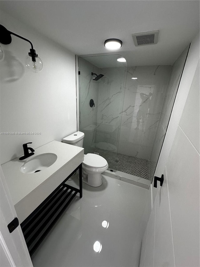 bathroom with a tile shower, sink, and toilet