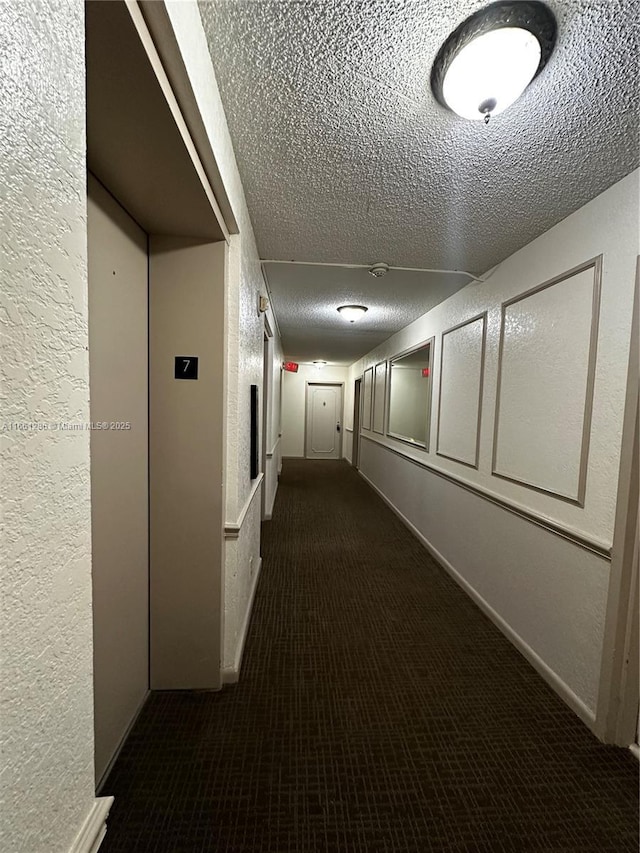 hallway with a textured ceiling and dark carpet