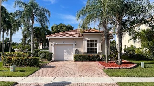 mediterranean / spanish house with a front yard, decorative driveway, stucco siding, an attached garage, and a tile roof