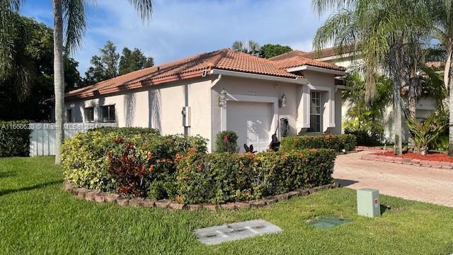view of side of home featuring a lawn, an attached garage, stucco siding, and a tile roof