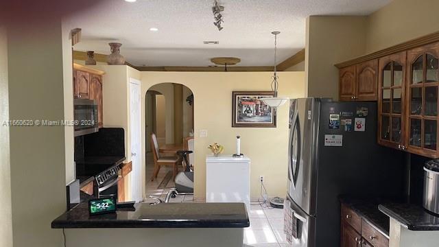 kitchen with dark countertops, arched walkways, stainless steel appliances, a peninsula, and glass insert cabinets