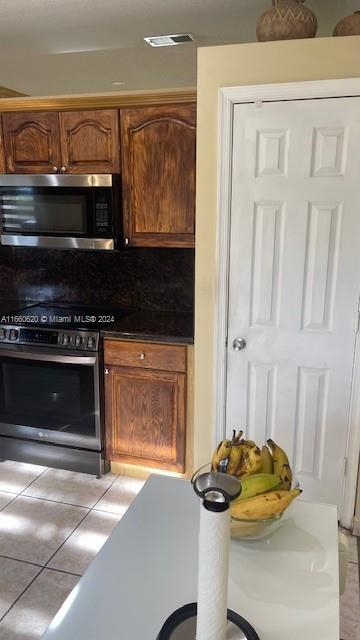 kitchen featuring visible vents, light tile patterned flooring, dark countertops, brown cabinets, and stainless steel appliances