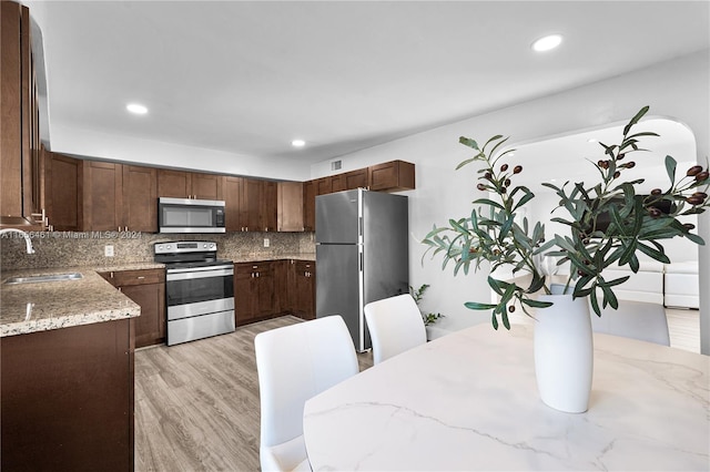 kitchen with light stone counters, sink, tasteful backsplash, appliances with stainless steel finishes, and light hardwood / wood-style floors