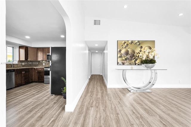 kitchen with light hardwood / wood-style floors, tasteful backsplash, stainless steel appliances, lofted ceiling, and dark brown cabinetry