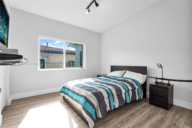 bedroom with wood-type flooring, lofted ceiling, and rail lighting