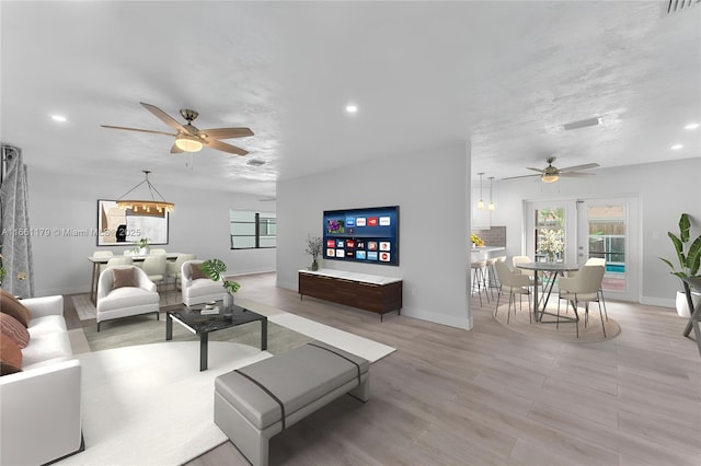 living room with a textured ceiling, light hardwood / wood-style flooring, and ceiling fan