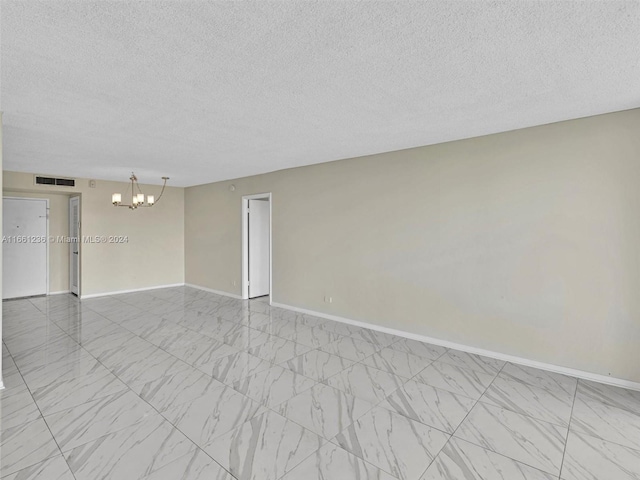 unfurnished room featuring a chandelier and a textured ceiling