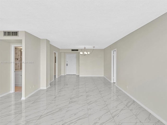 unfurnished room with a notable chandelier and a textured ceiling