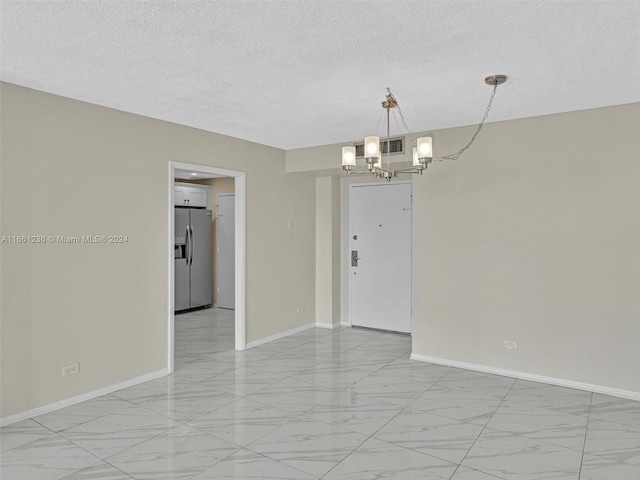 spare room featuring a notable chandelier and a textured ceiling