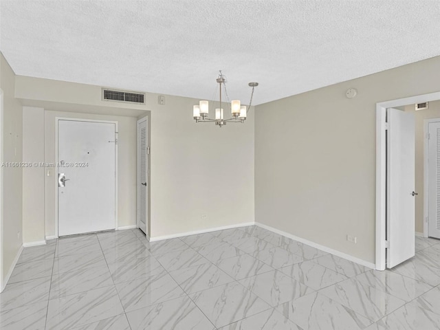 empty room featuring a textured ceiling and an inviting chandelier