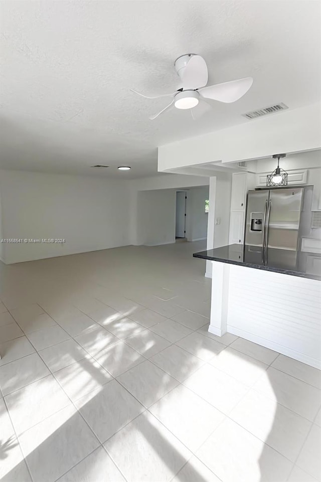 interior space featuring ceiling fan, white cabinets, light tile patterned flooring, a textured ceiling, and stainless steel refrigerator with ice dispenser