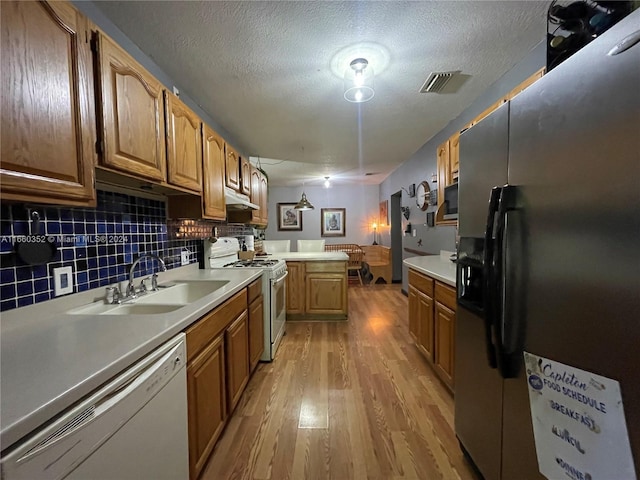 kitchen featuring sink, white appliances, tasteful backsplash, a textured ceiling, and light hardwood / wood-style flooring