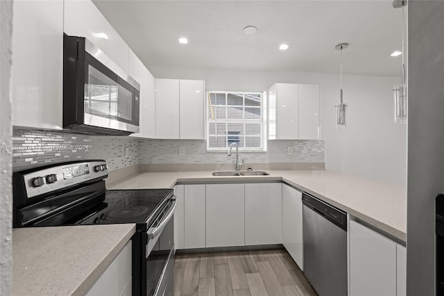 kitchen with appliances with stainless steel finishes, white cabinetry, pendant lighting, light wood-type flooring, and sink