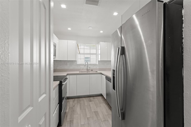 kitchen featuring appliances with stainless steel finishes, white cabinets, backsplash, light hardwood / wood-style flooring, and sink