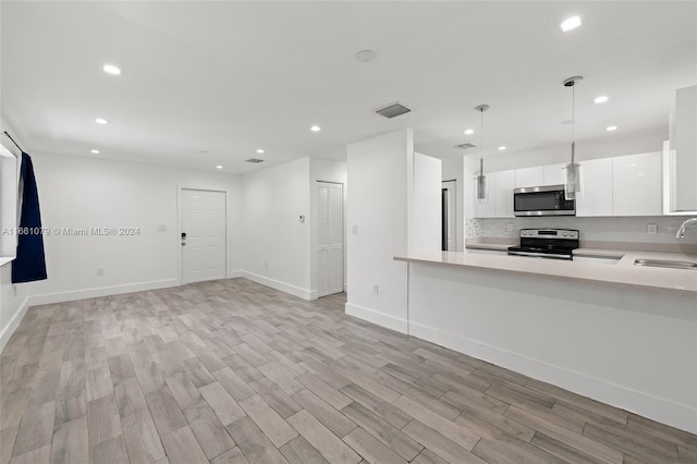 kitchen with pendant lighting, white cabinets, sink, stainless steel appliances, and light wood-type flooring