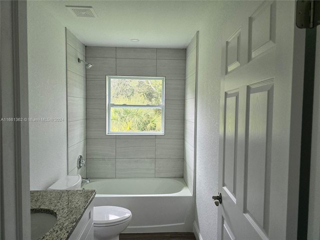 full bathroom featuring vanity, tiled shower / bath combo, and toilet