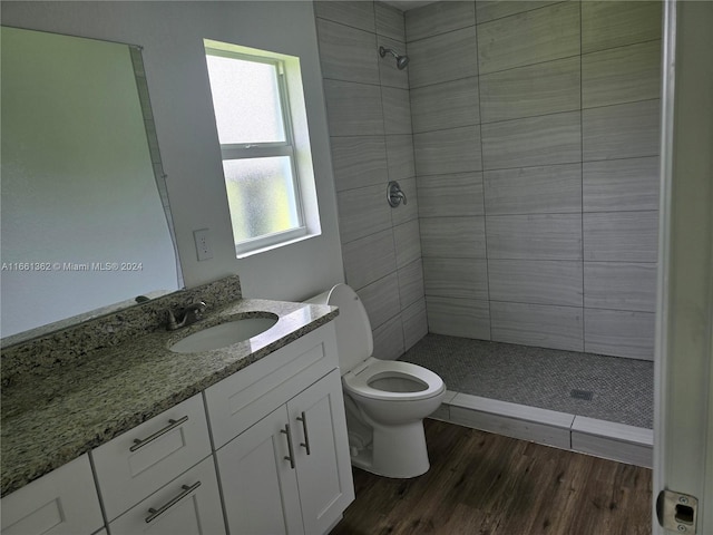 bathroom featuring wood-type flooring, tiled shower, vanity, and toilet