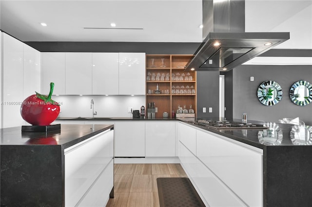 kitchen with dark stone countertops, white cabinetry, island range hood, black gas stovetop, and sink