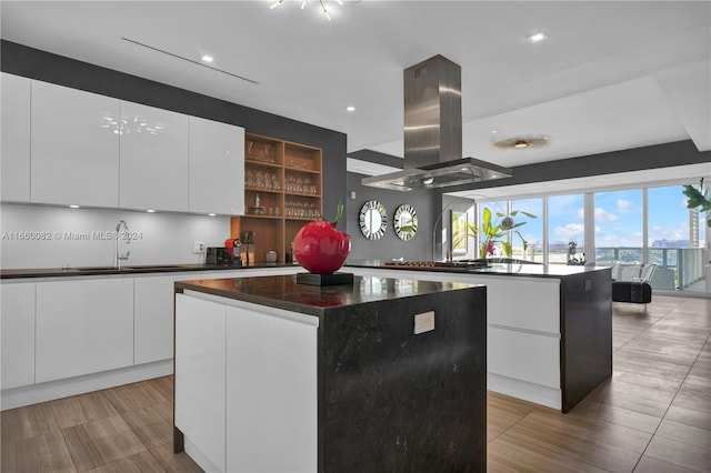 kitchen featuring white cabinets, sink, a kitchen island, island range hood, and stainless steel gas stovetop