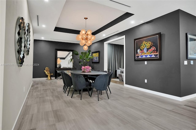 dining space with a tray ceiling, light hardwood / wood-style flooring, and a notable chandelier