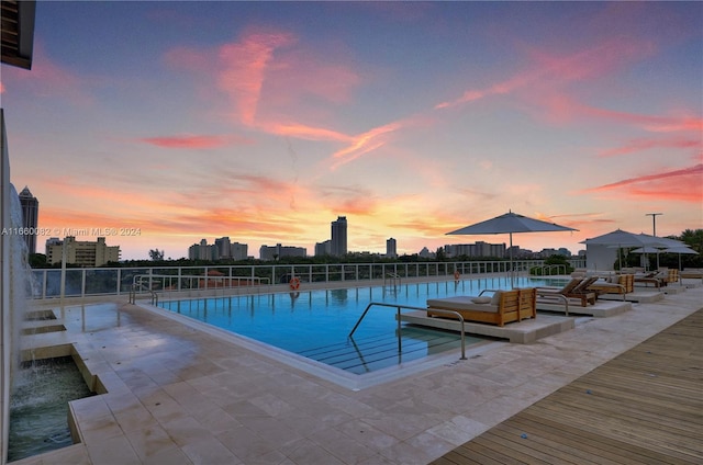 pool at dusk featuring a water view and a patio area