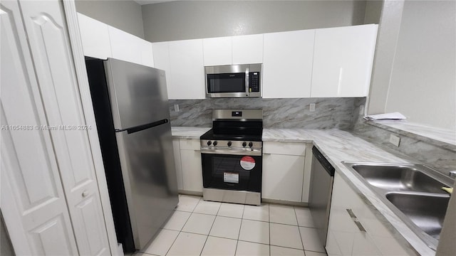 kitchen featuring stainless steel appliances, sink, light tile patterned floors, white cabinetry, and tasteful backsplash