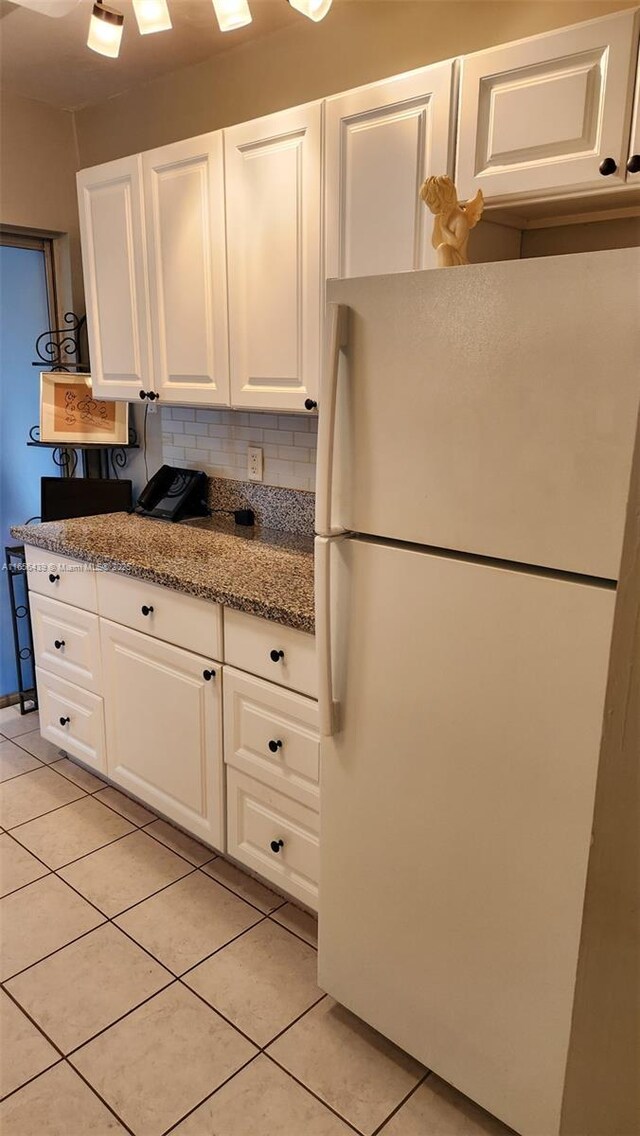 kitchen with white cabinetry, white fridge, decorative backsplash, light tile patterned flooring, and stone counters