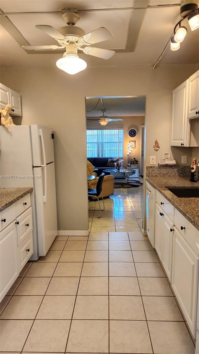 kitchen with light tile patterned flooring, dark stone countertops, white cabinets, and white appliances