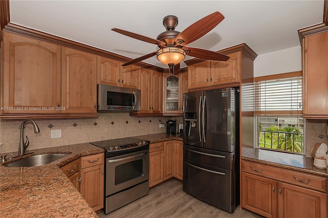 kitchen with ceiling fan, sink, light hardwood / wood-style flooring, stainless steel appliances, and dark stone countertops