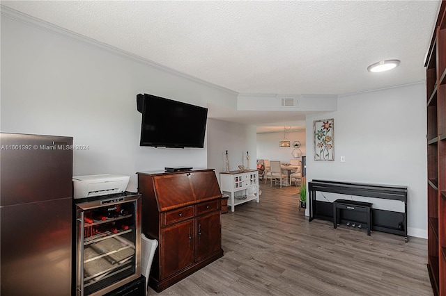 office area with a textured ceiling, light hardwood / wood-style flooring, beverage cooler, and ornamental molding