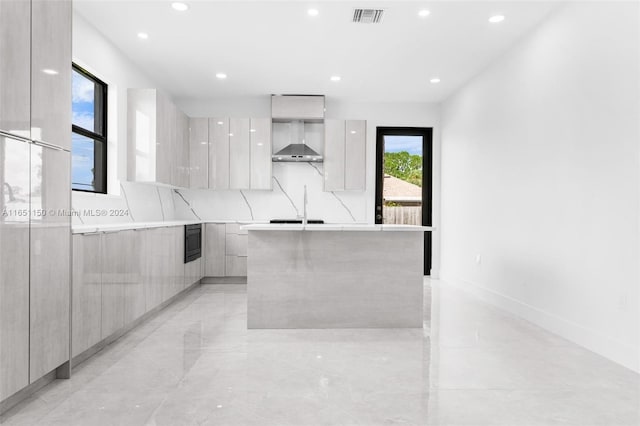 kitchen with an island with sink, tasteful backsplash, and wall chimney range hood