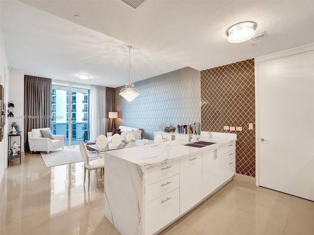 kitchen featuring light stone counters, white cabinets, sink, kitchen peninsula, and decorative light fixtures