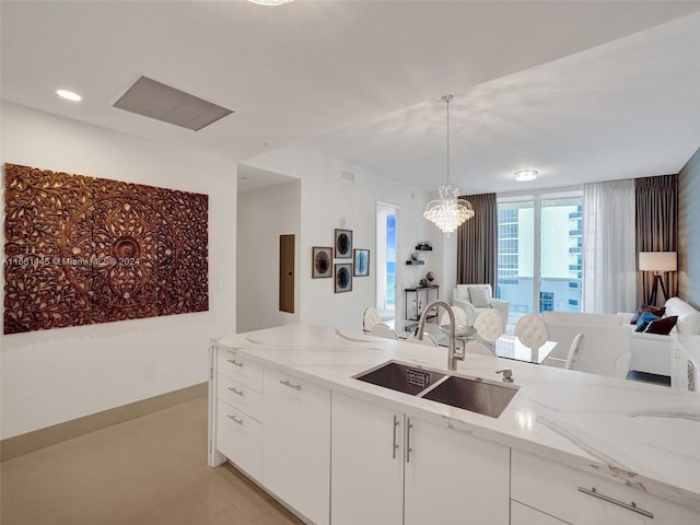 kitchen with light stone counters, white cabinets, hanging light fixtures, and sink