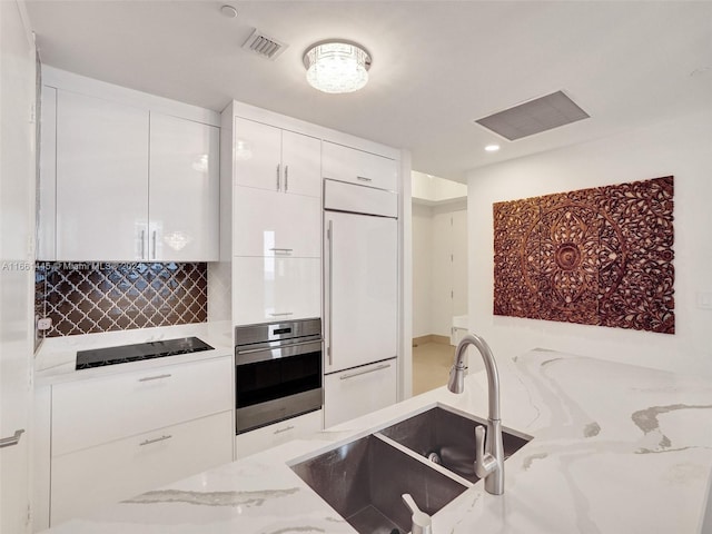 kitchen featuring black electric cooktop, light stone counters, white cabinets, oven, and sink