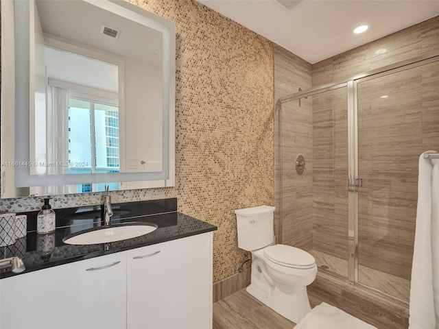 bathroom with hardwood / wood-style flooring, walk in shower, vanity, and toilet