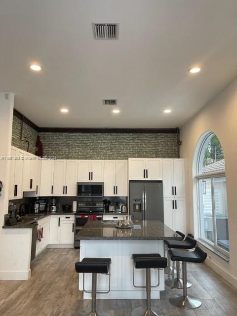 kitchen with refrigerator with ice dispenser, white cabinetry, a center island, and black stove