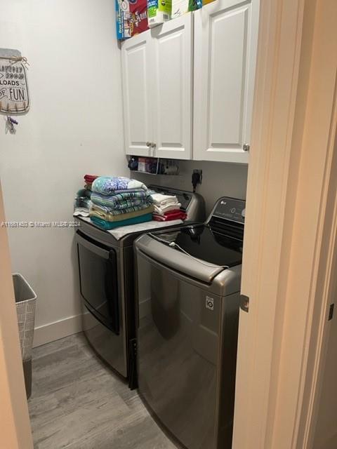 laundry area with washer and clothes dryer, light hardwood / wood-style flooring, and cabinets