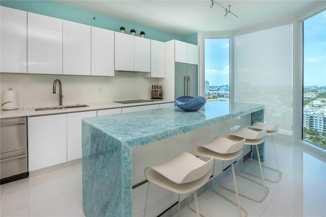 kitchen featuring sink, built in refrigerator, white cabinetry, black electric cooktop, and a breakfast bar