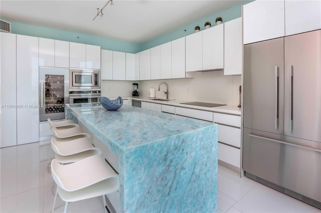 kitchen with built in appliances, white cabinetry, a breakfast bar area, and sink