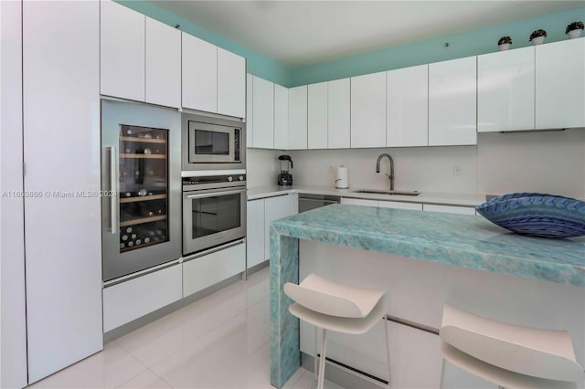 kitchen featuring appliances with stainless steel finishes, white cabinetry, sink, and wine cooler