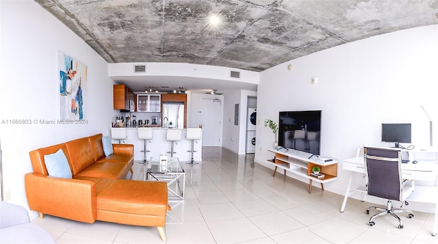 living room with stacked washer / dryer, light tile patterned flooring, and bar area