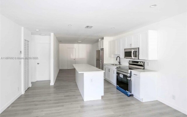 kitchen featuring light wood-type flooring, a center island, sink, white cabinets, and stainless steel appliances