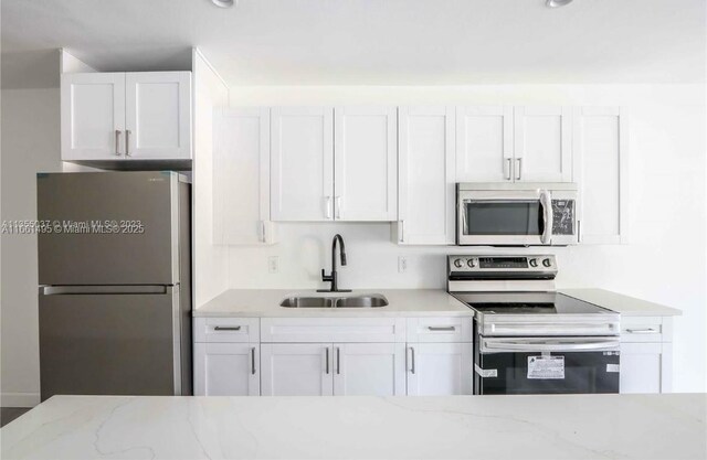 kitchen with stainless steel appliances, white cabinetry, light stone counters, and sink