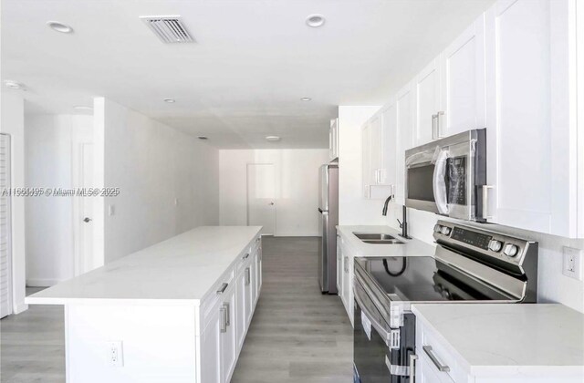 kitchen featuring appliances with stainless steel finishes, white cabinetry, light wood-type flooring, a center island, and sink