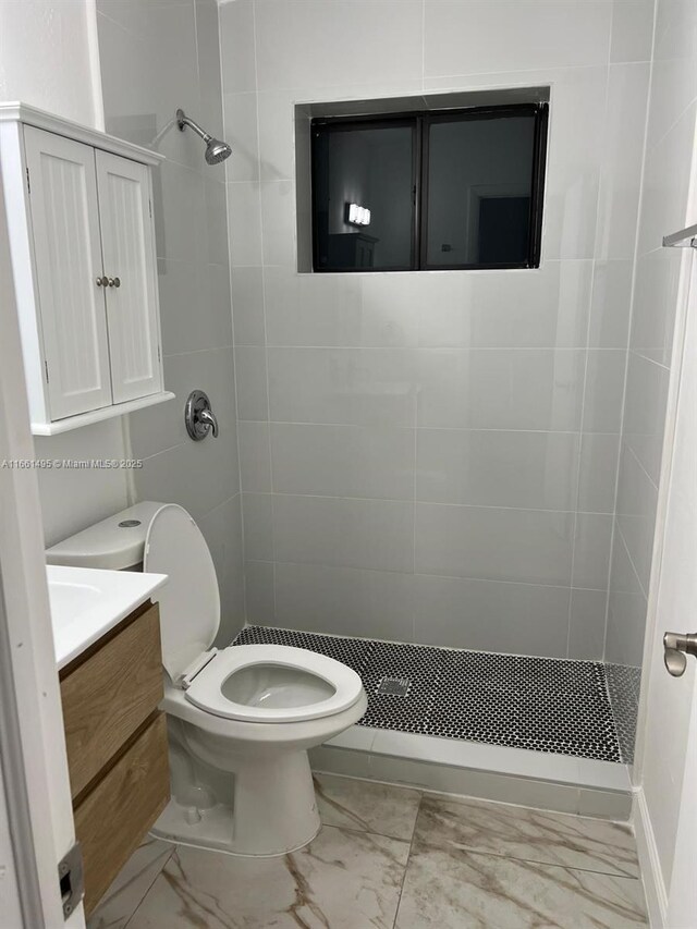 bathroom with a tile shower, vanity, and toilet