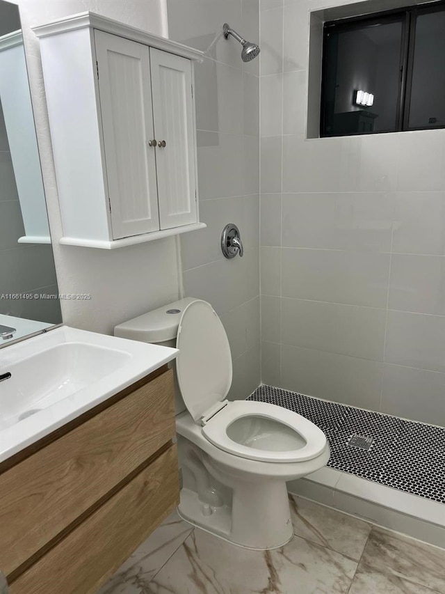 bathroom with a tile shower, vanity, and toilet