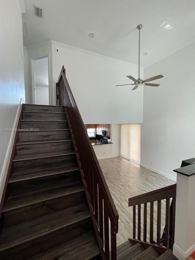 stairway featuring wood-type flooring, ornamental molding, and ceiling fan