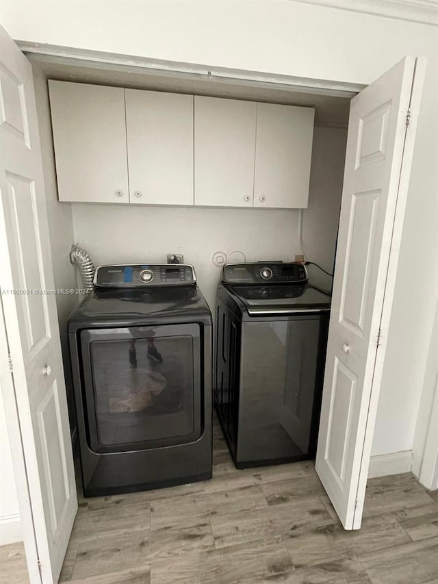 clothes washing area featuring washer and clothes dryer, light hardwood / wood-style floors, and cabinets